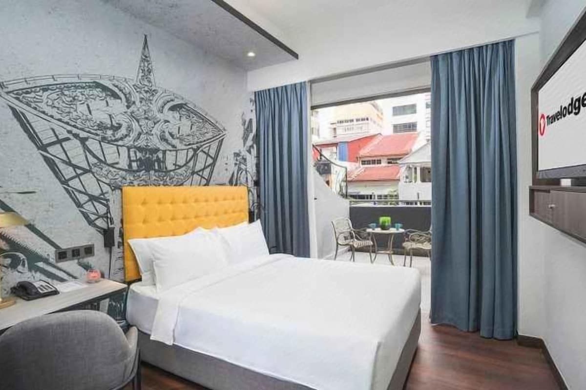Een hotelkamer met een bed, een bureau, een stoel, een raam met gordijnen en een muur met een muurschildering.