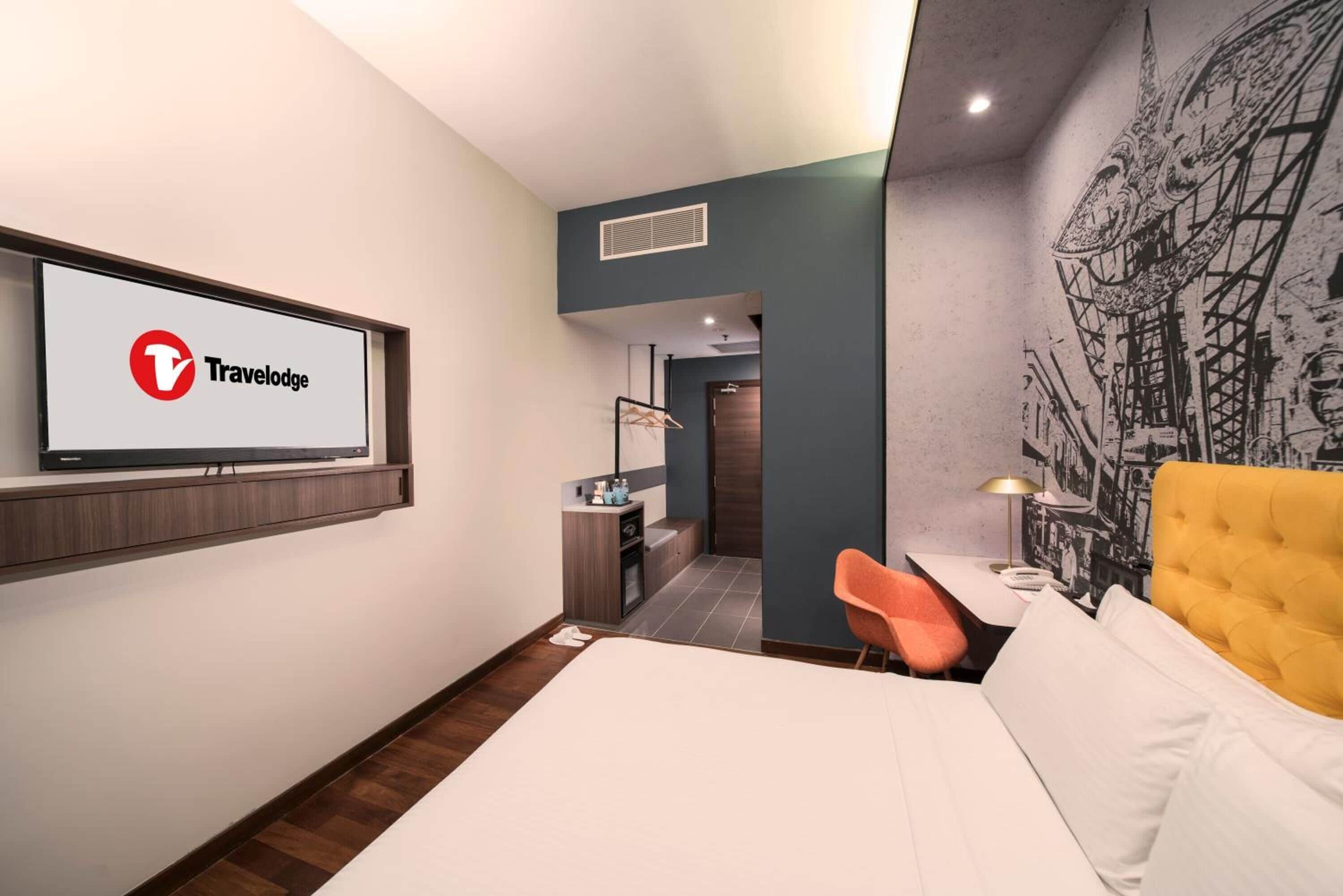 Una habitación de hotel moderna con una cama, un escritorio con silla, un televisor en la pared y un mural.