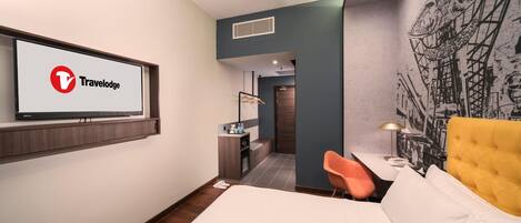 Una habitación de hotel moderna con una cama, un escritorio con silla, un televisor en la pared y un mural.