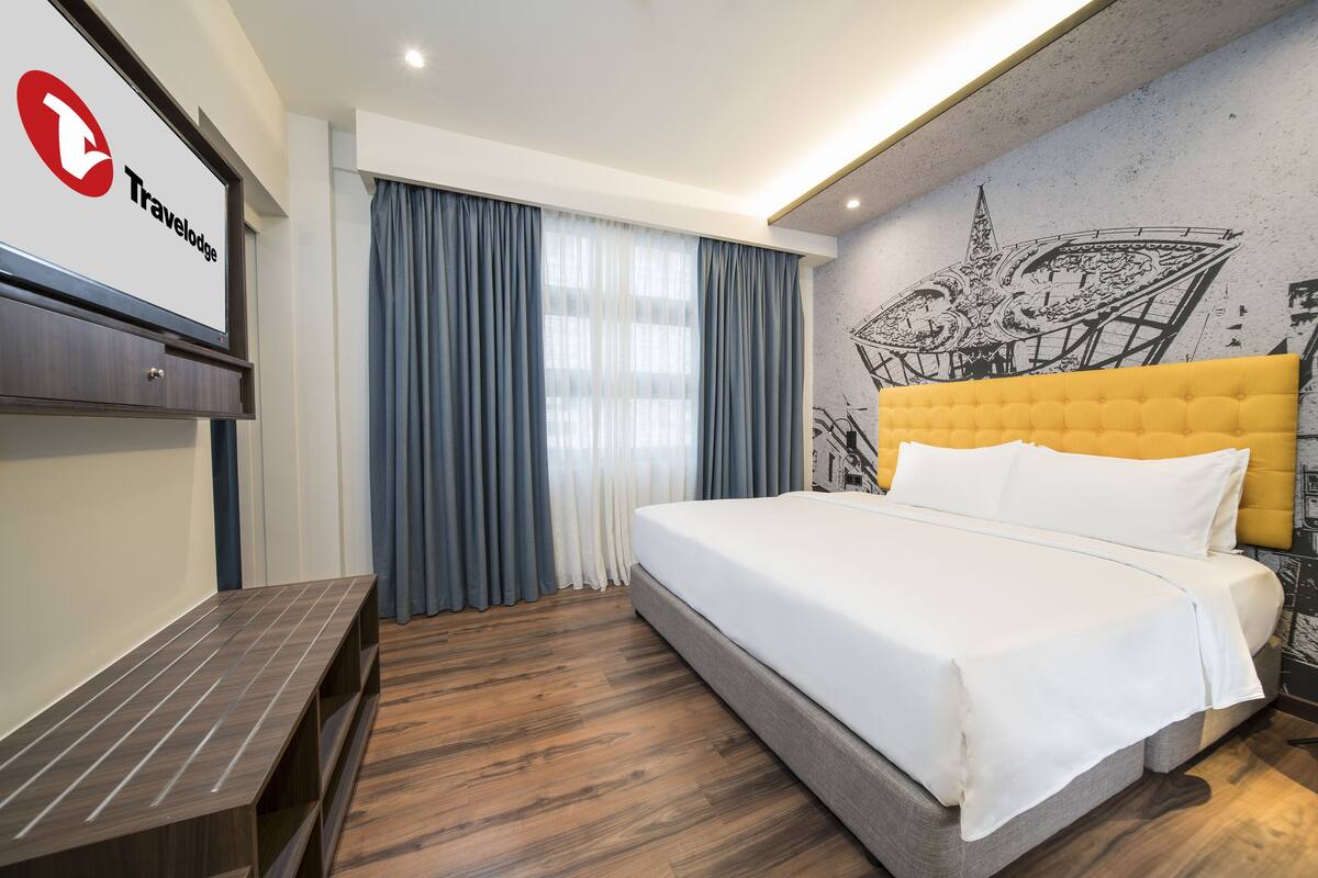 Une chambre d’hôtel avec un lit, un banc, un panneau fixé au mur et une grande fenêtre avec des rideaux.