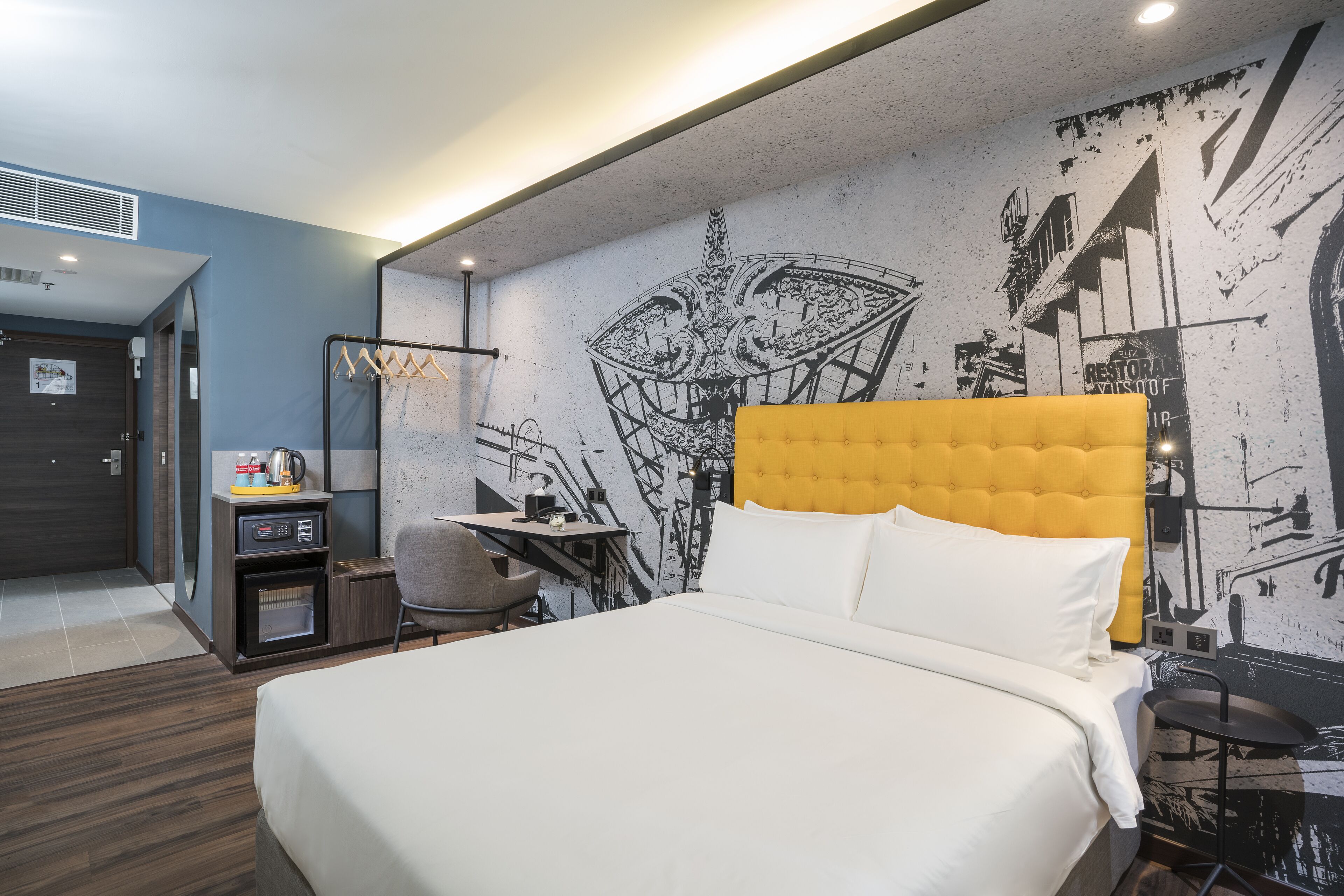 A hotel room with a large bed, a desk, a chair, and a wall mural.