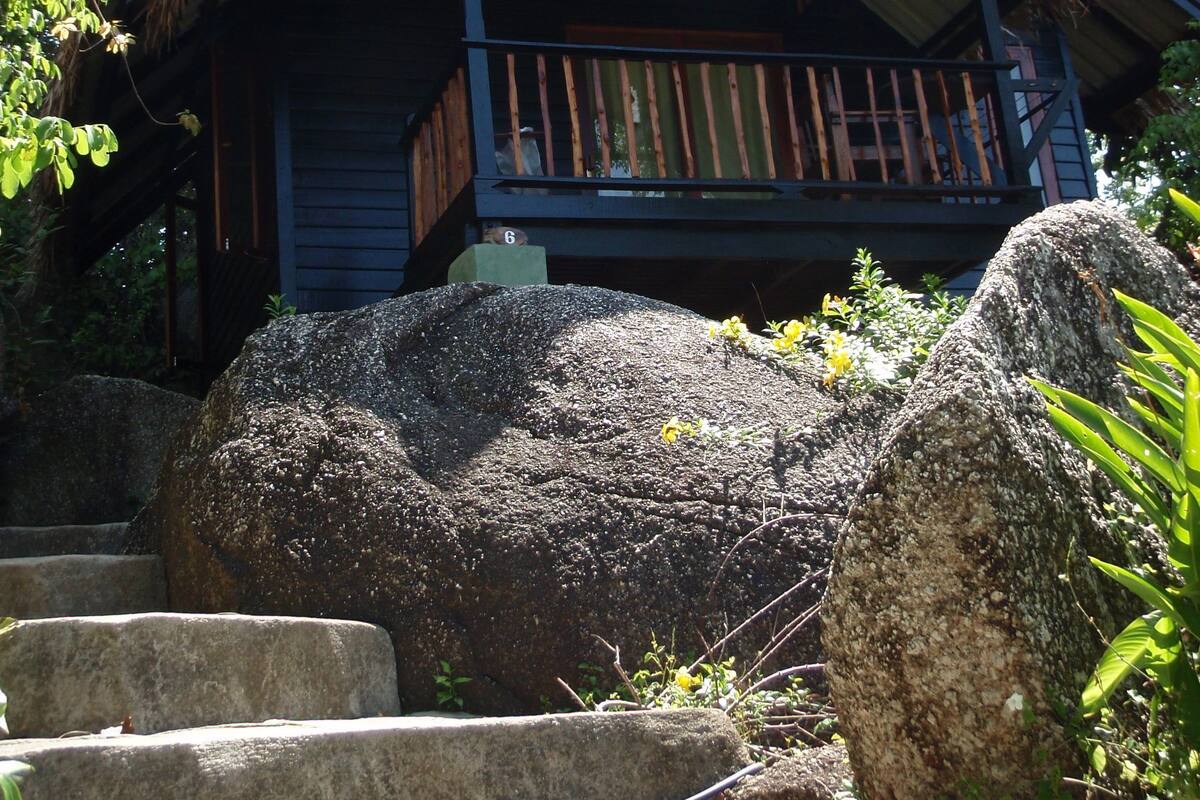 Una casa con balcón, rodeada de grandes rocas y follaje.