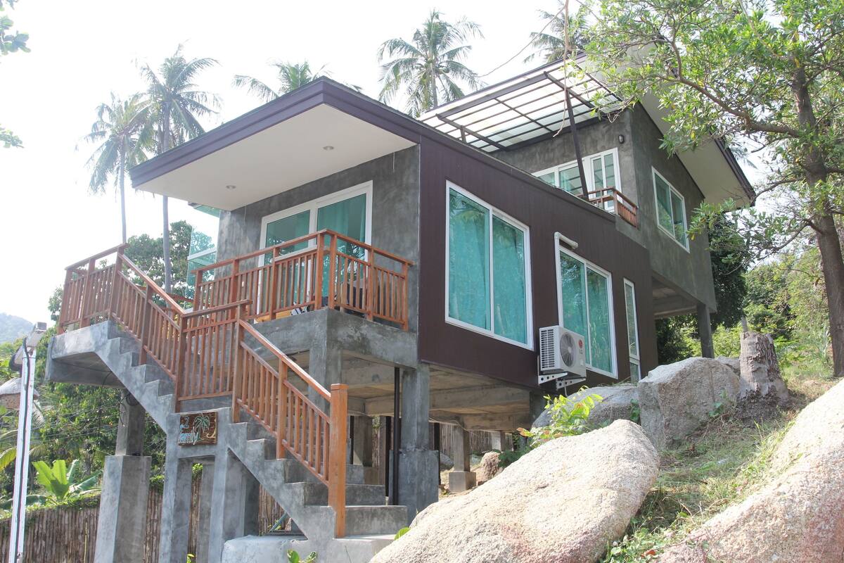 Una casa moderna de dos pisos con balcón, ventanas grandes y una escalera.
