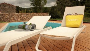 Zona de piscina con dos sillas de descanso, una con cojín amarillo que dice "Summer" y una pared de piedra al fondo.