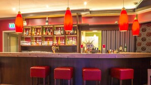 Una zona de bar con mostrador de madera, taburetes rojos y lámparas colgantes rojas.