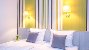 Habitación de hotel con dos camas, cada una con ropa blanca y almohadas grises, y una pared con rayas verticales amarillas y blancas.