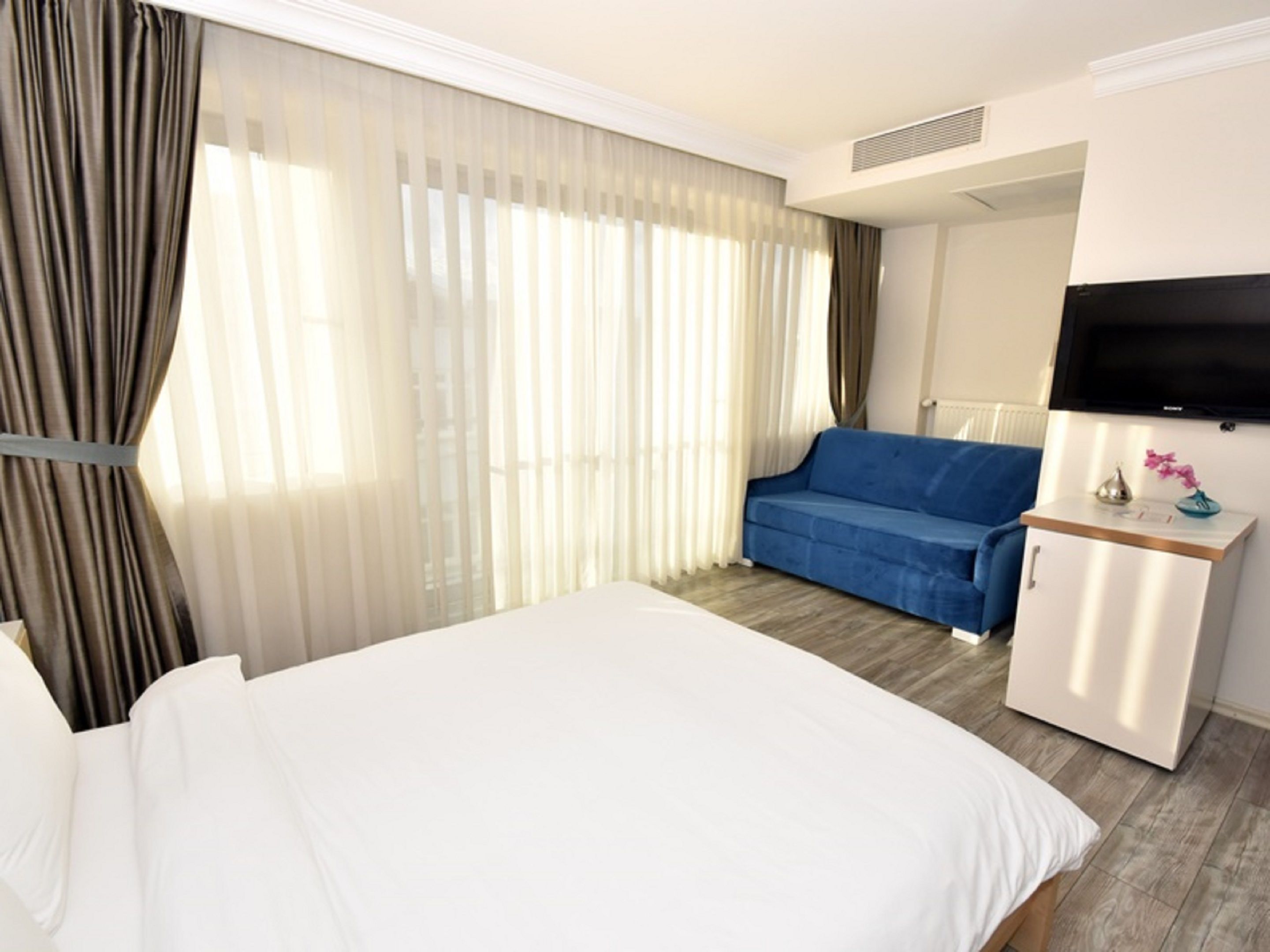 A hotel room with a large bed, a blue sofa, a TV, and a desk with a vase of flowers.