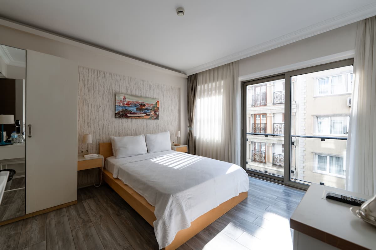 Habitación de hotel moderna con una cama grande, un escritorio y un balcón con vistas a la ciudad.