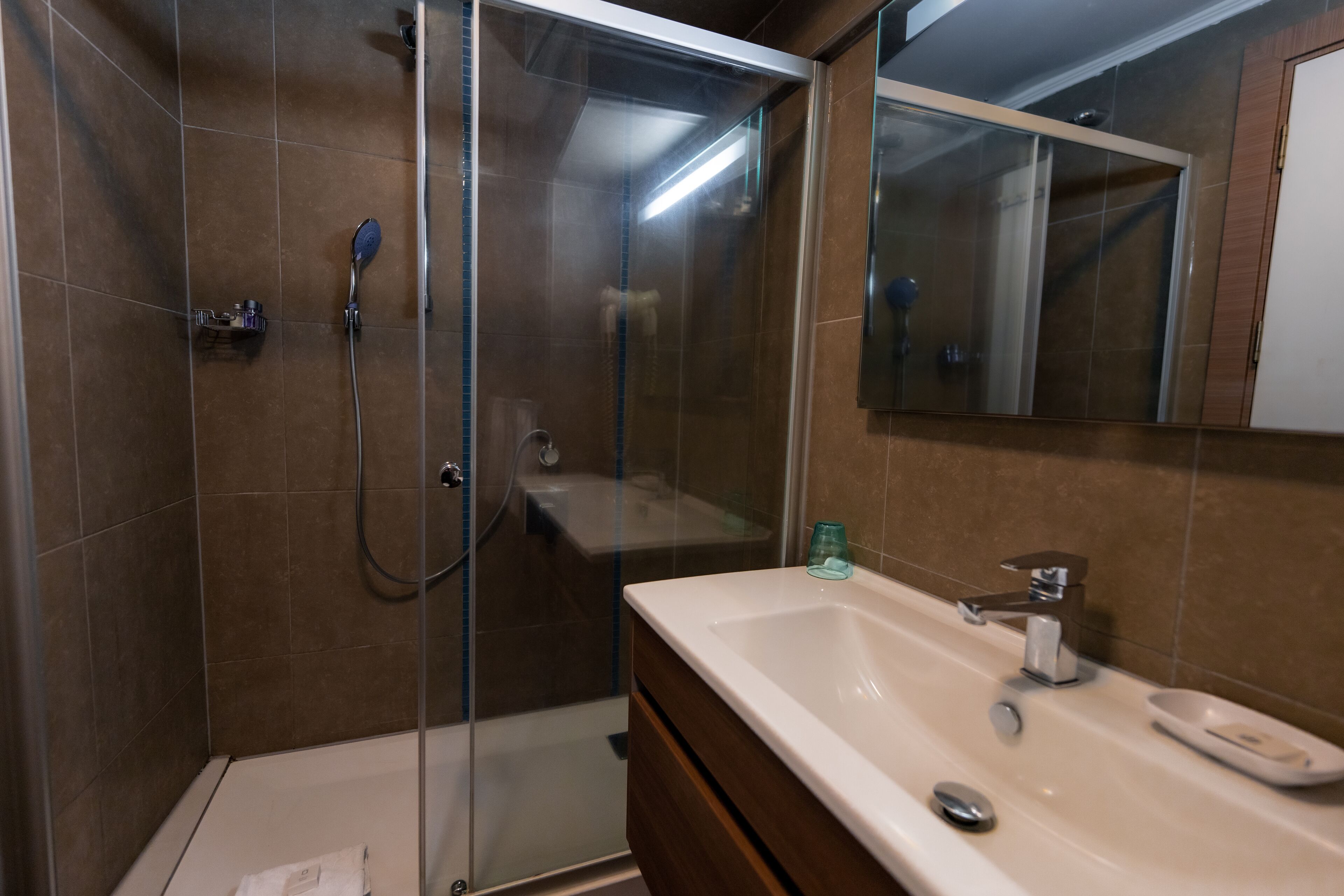 A bathroom with a glass-enclosed shower, a sink with a mirror, and a cabinet.