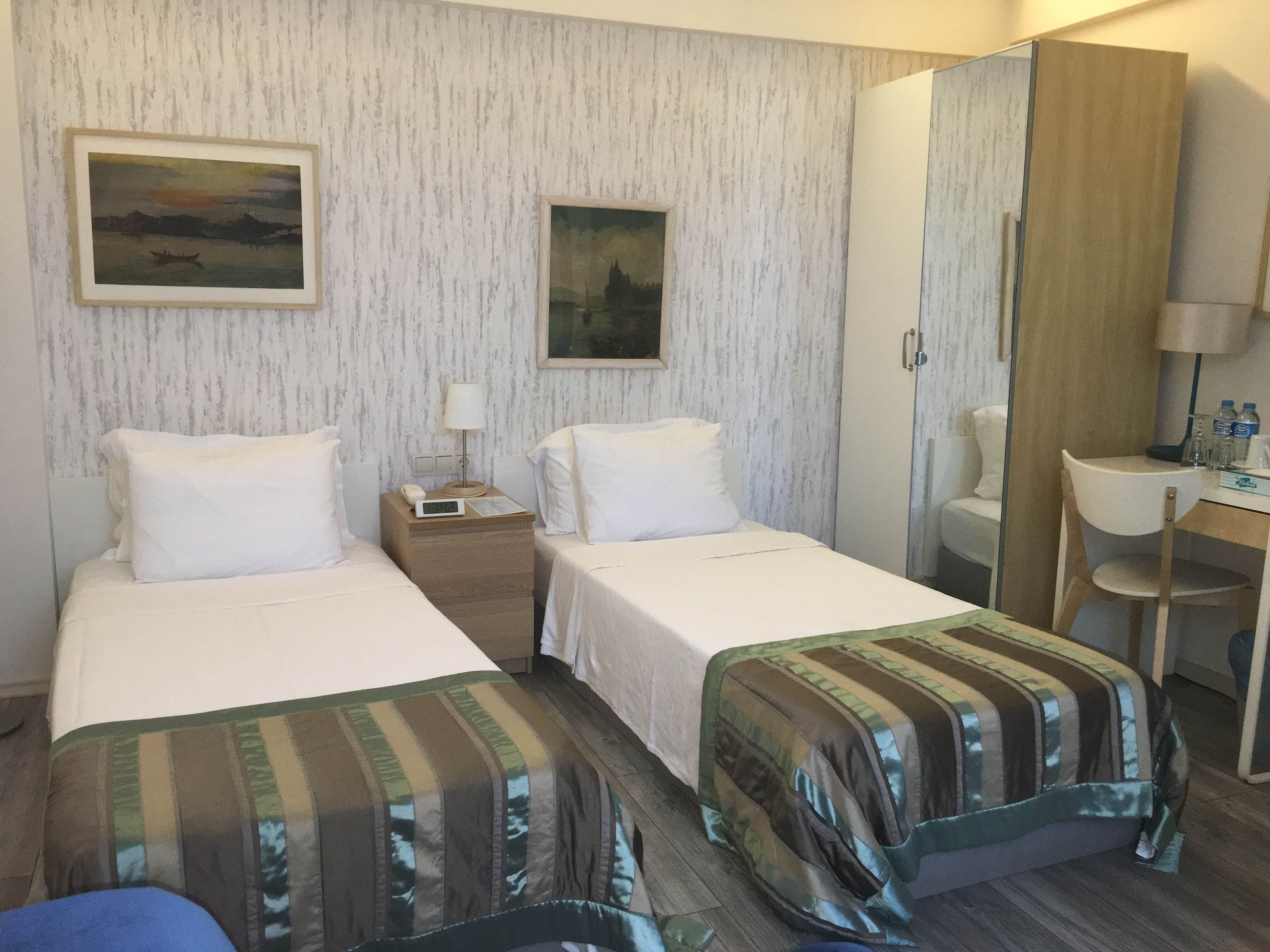 A hotel room with two beds, a desk, a chair, and a wardrobe.
