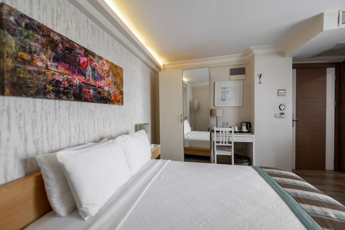 Habitación de hotel con cama, escritorio, silla, espejo y un cuadro en la pared.
