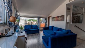 Una sala de estar moderna con un sofá azul, una mesa de comedor con sillas y vistas a la ciudad a través de amplias ventanas.
