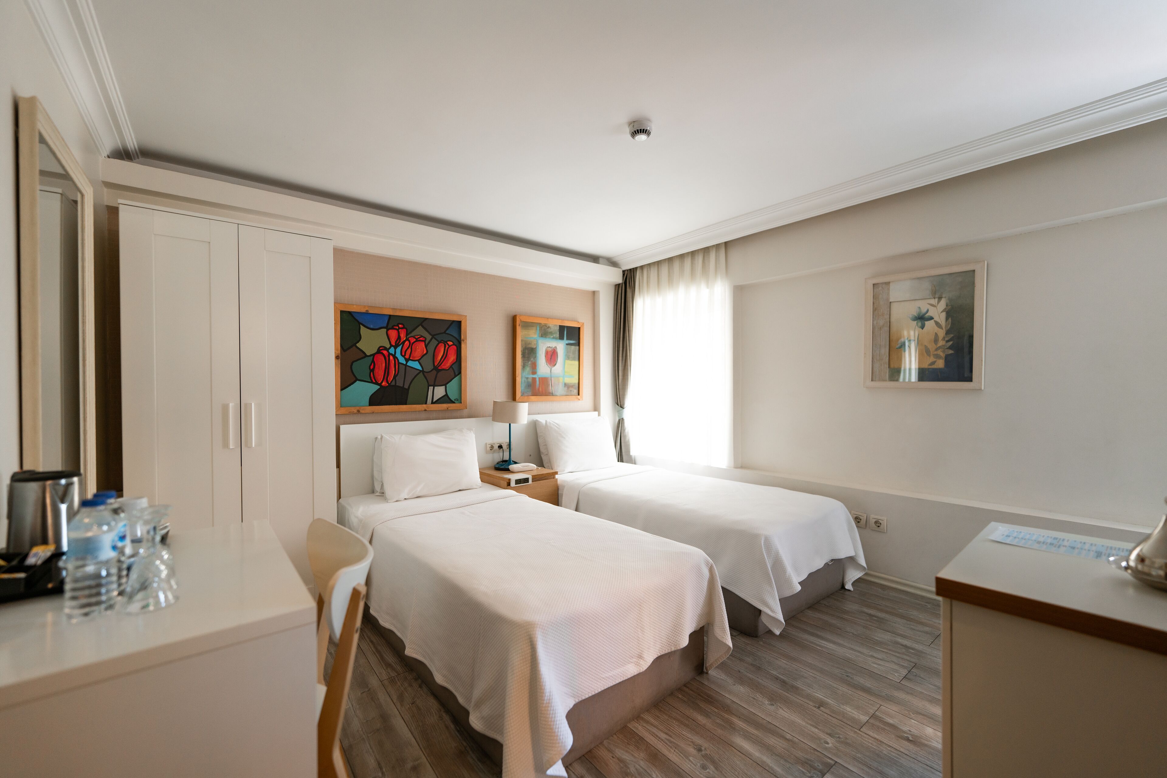 Een hotelkamer met twee bedden, een bureau met stoel, een kledingkast en kunstwerken aan de muren.