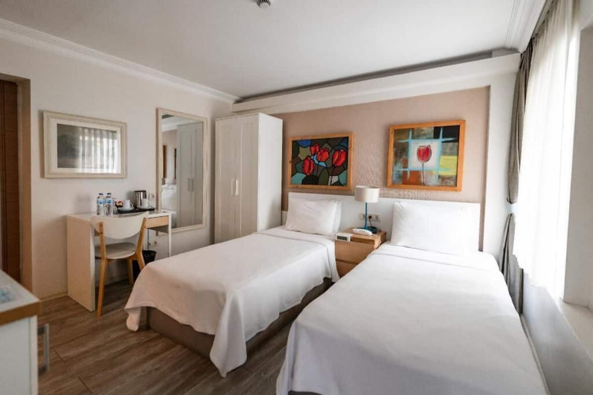 Habitación de hotel con dos camas, un escritorio, una silla y obras de arte en las paredes.