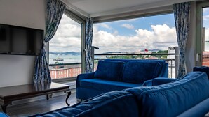 Una habitación con sofá azul, televisor de pantalla plana y balcón con vista a la ciudad y al agua.