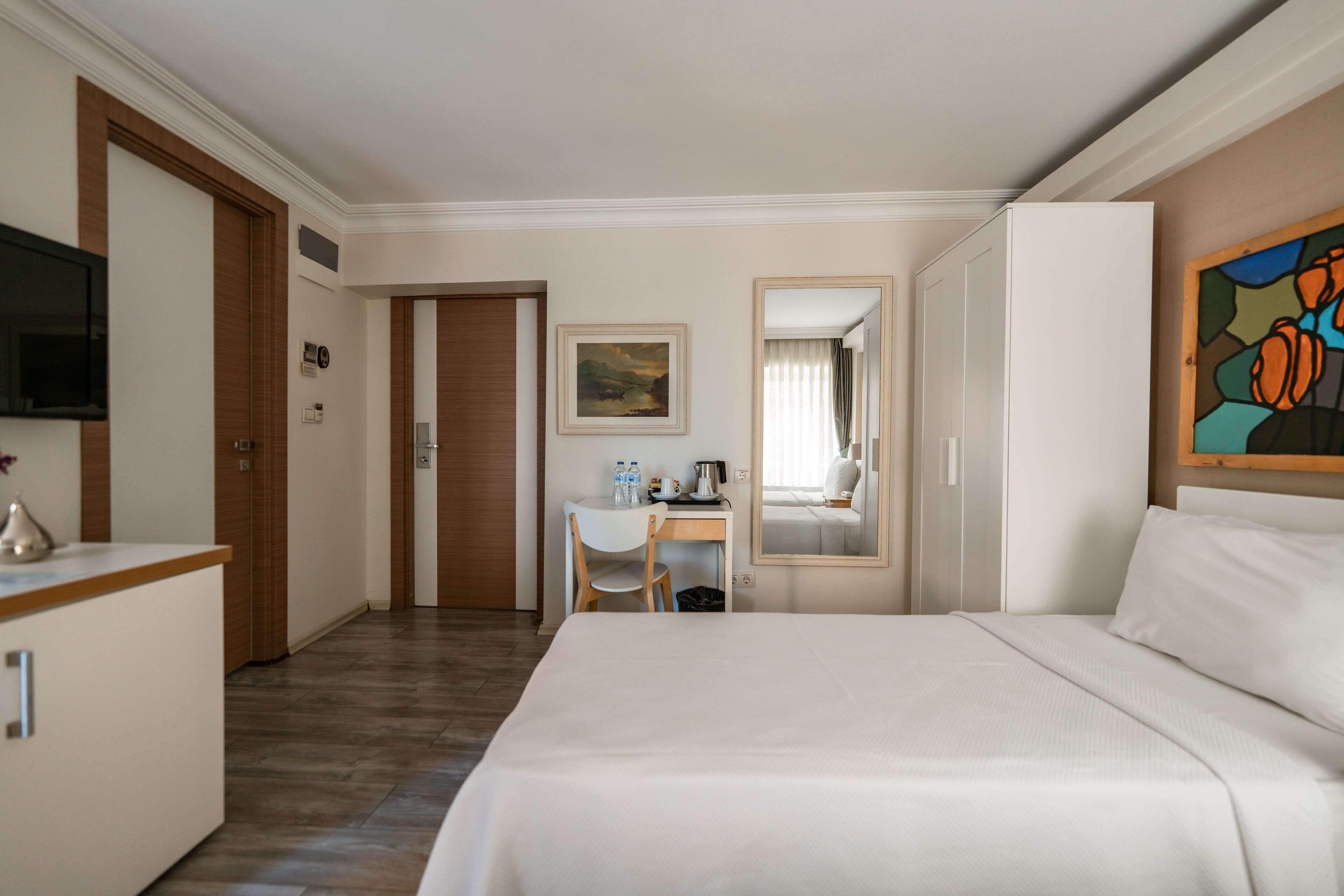 A hotel room with a bed, a desk, a chair, a TV, and a painting on the wall.