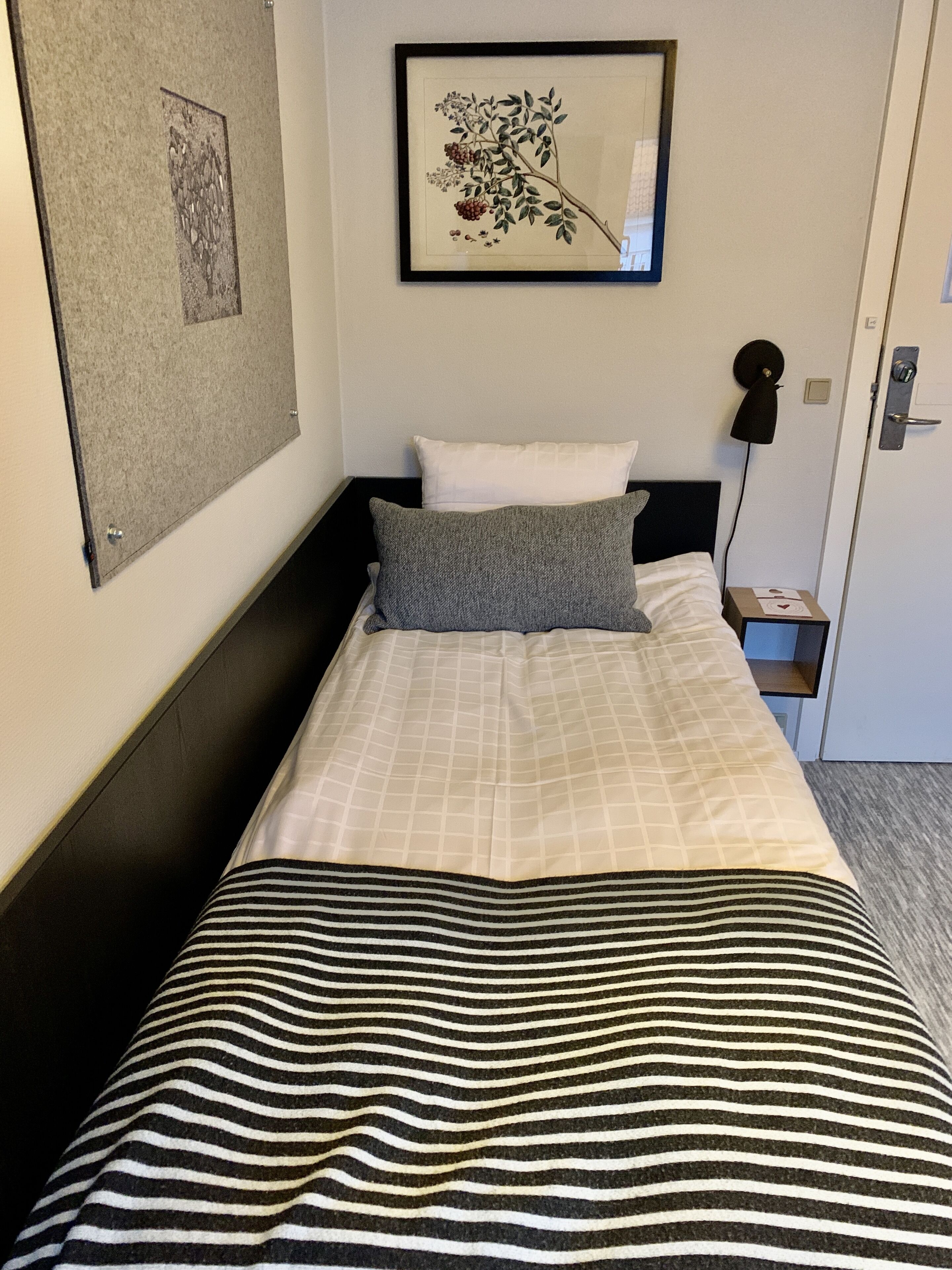 Una cama bien hecha con un edredón a rayas, una almohada e impresión enmarcadas de motivos botánicos en la pared.