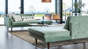 A modern living room with a green sofa, a matching ottoman, and a coffee table. There is a large window with a view of the outdoors. - Rungstedgaard (Rungsted Kyst)