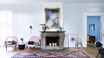 Una habitación con chimenea, dos sillas rosas, una alfombra estampada y un cuadro en la pared.