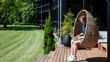 A person sitting in a wicker swing chair on a wooden deck, using a laptop.