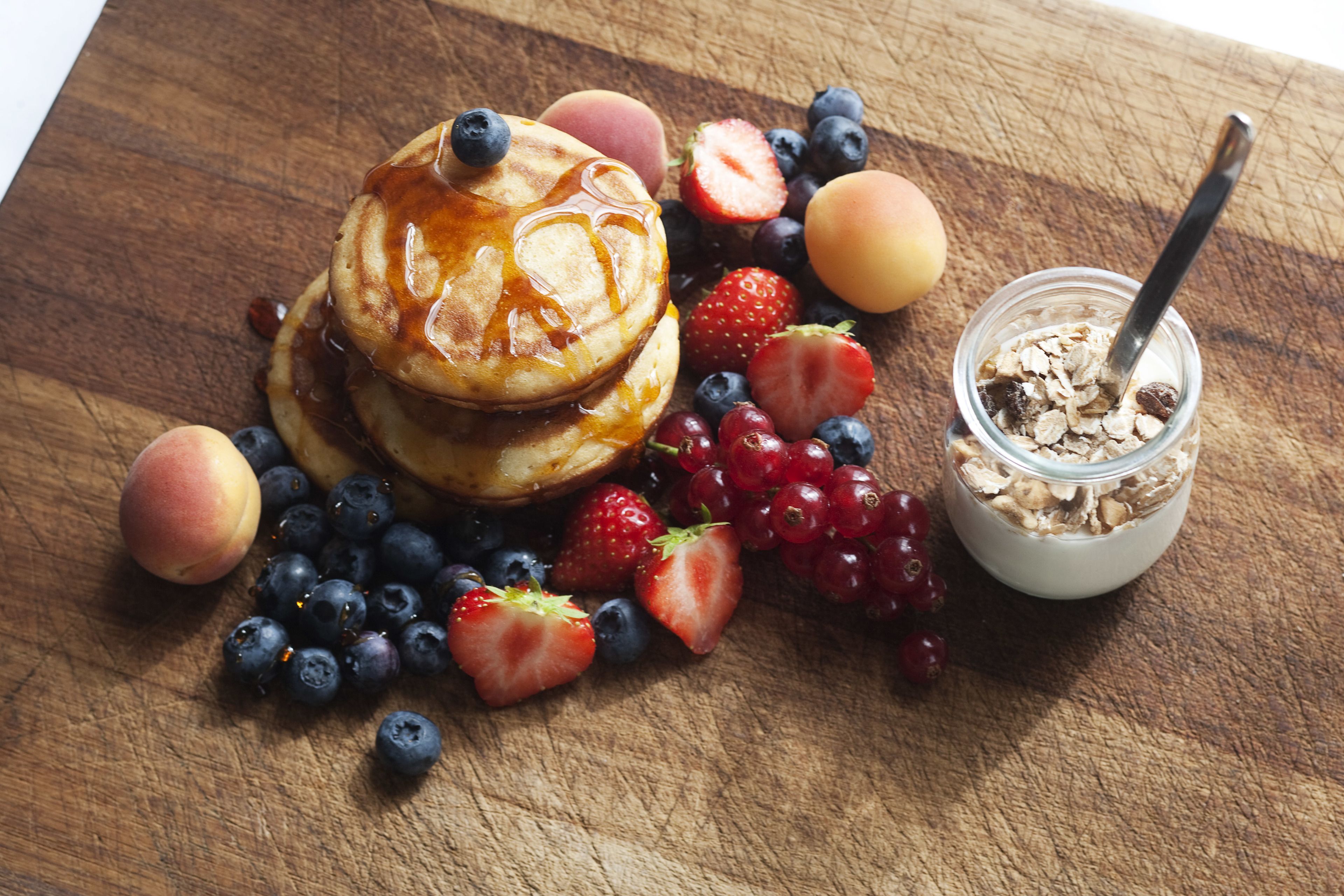 Ein Holztisch mit Pfannkuchen, Erdbeeren, Blaubeeren und einem Getreidegläschen.
