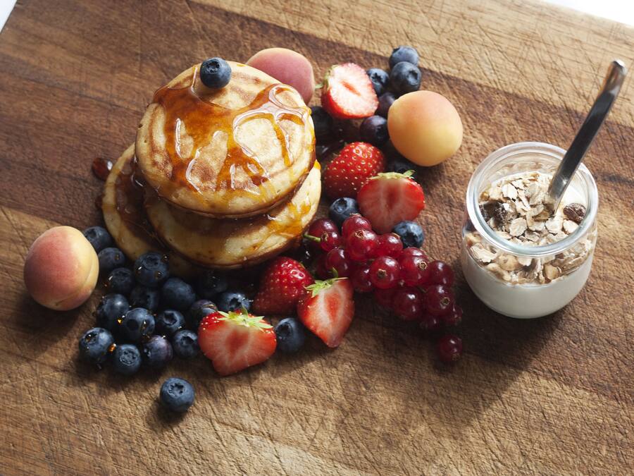 Una mesa de madera con panqueques, fresas, arándanos y un frasco de cereal.