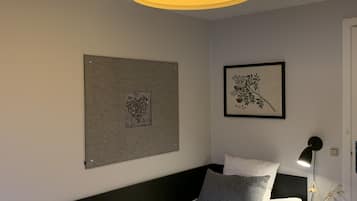 Un dormitorio ordenado con una cama, una mesita de noche con lámpara y dos cuadros enmarcados en la pared.