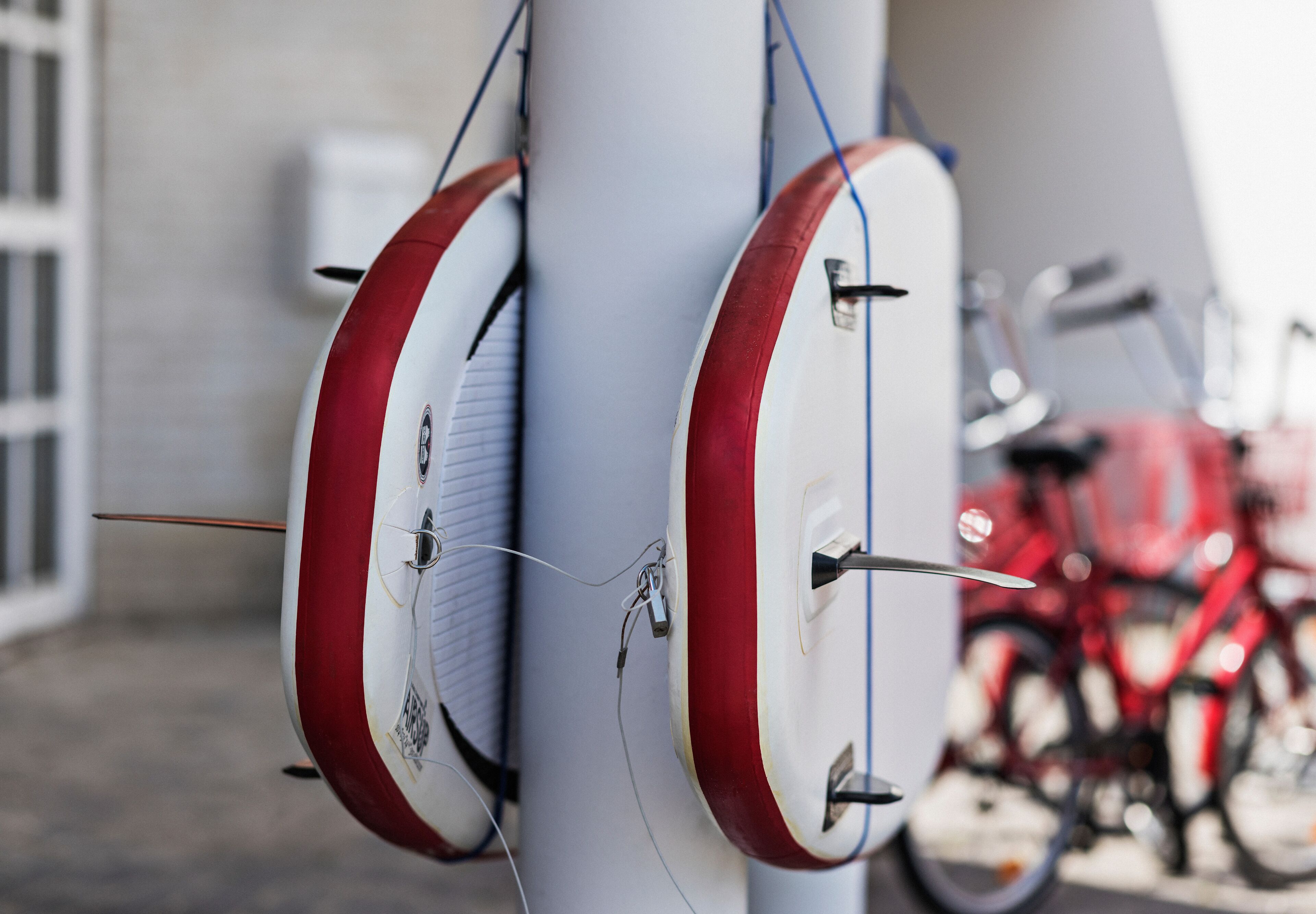 Un portaequipajes para tablas de surf con varias tablas, una bicicleta roja al fondo y una pared blanca.