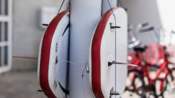 Un portaequipajes para tablas de surf con varias tablas, una bicicleta roja al fondo y una pared blanca.