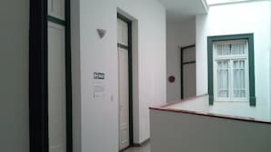 A corridor with white walls, green door frames, and a window with white curtains. - Hotel del Prado (Buenos Aires)