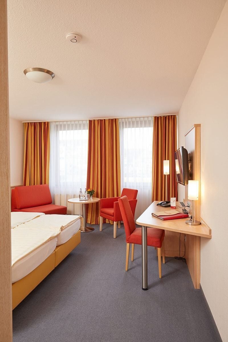 A hotel room with a bed, a desk, a chair, a television, and curtains.