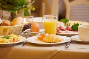 Une table mise pour le petit-déjeuner avec des assiettes de nourriture, un verre de jus d’orange et un croissant.