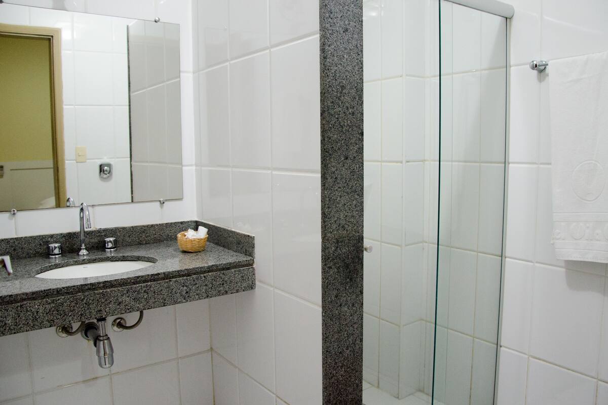 Une salle de bain avec un lavabo surmonté d’un plan de travail en granit, un miroir et une cabine de douche en verre.
