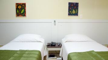 Una habitación de hotel con dos camas individuales, una mesita de noche con teléfono y control remoto, y dos cuadros en la pared.