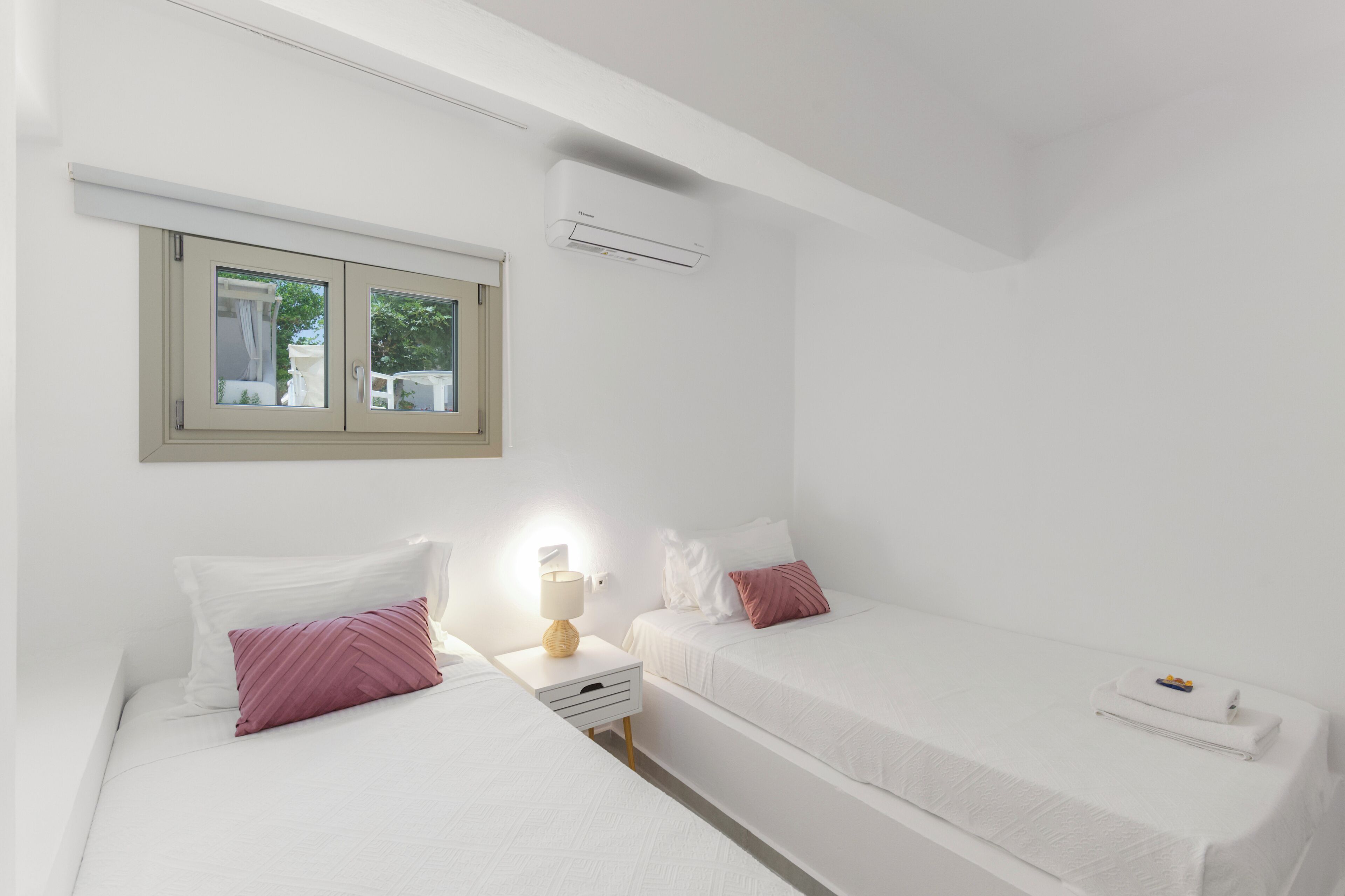 Een slaapkamer met twee bedden, een raam, een airconditioner en een bedlampje.