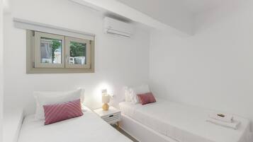 Een slaapkamer met twee bedden, een raam, een airconditioner en een bedlampje.