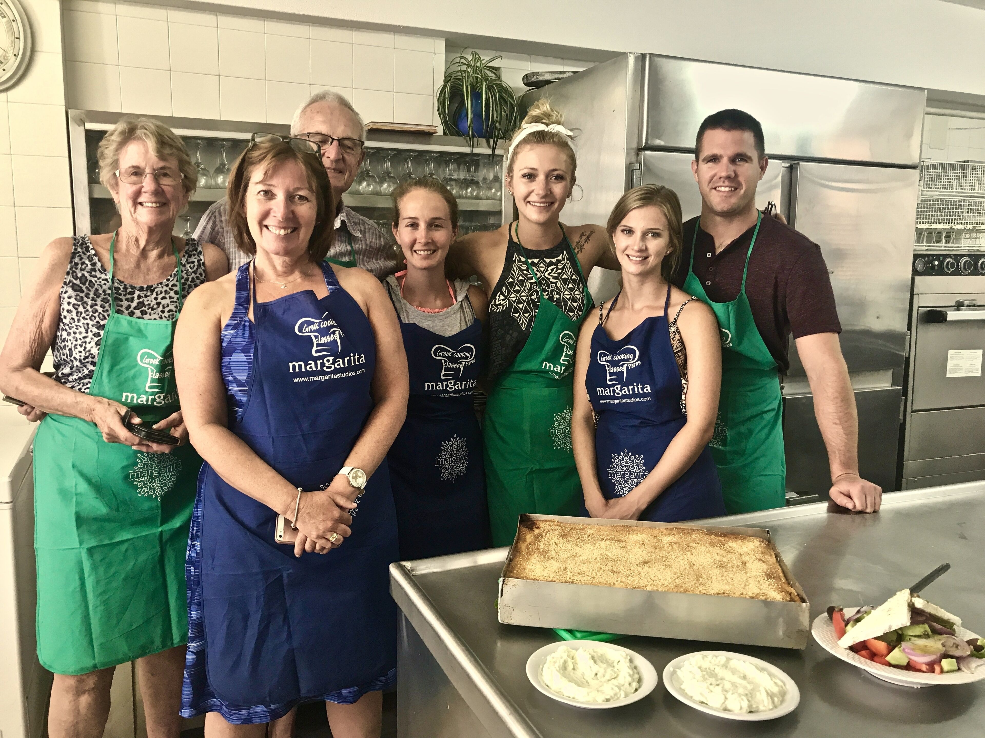 A group of people in a kitchen with aprons, a tray of food, and a refrigerator.