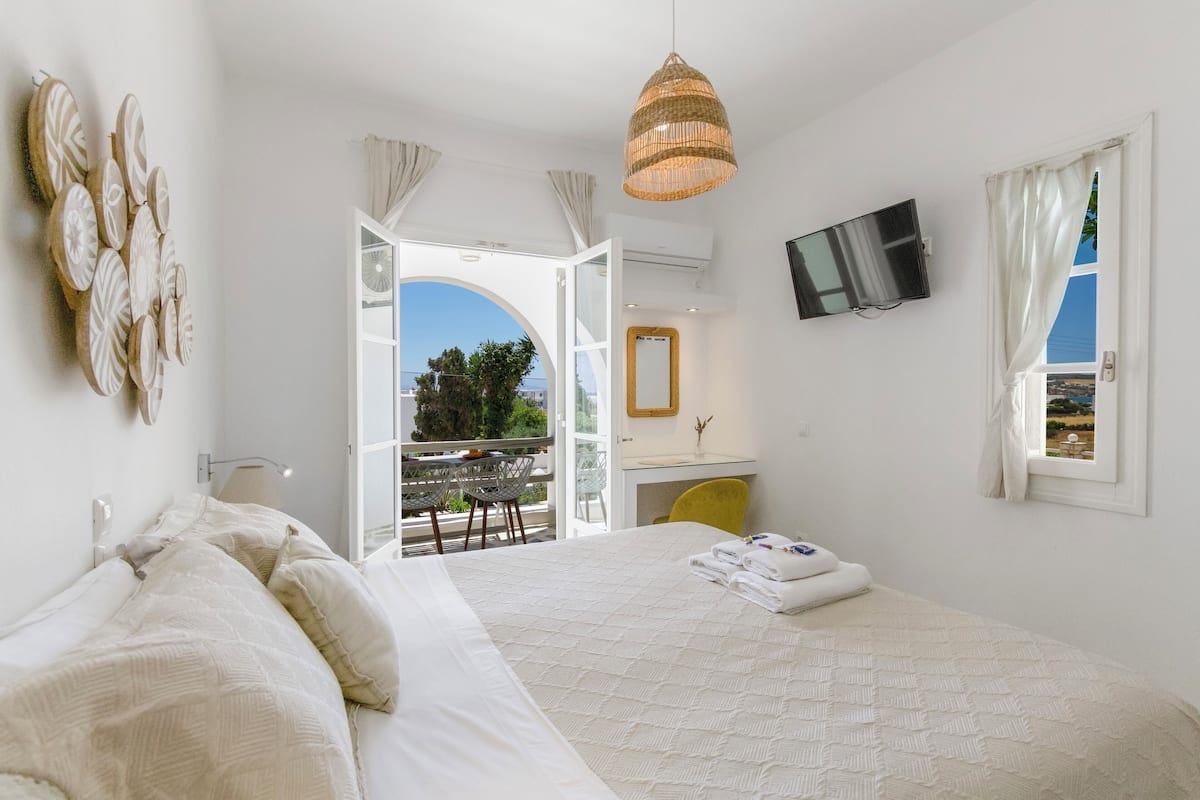 Ein Hotelzimmer mit einem großen Bett, einem Schreibtisch, einem Fernseher und einem Balkon mit Blick.