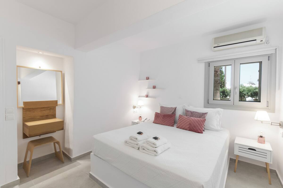 Ein modernes Schlafzimmer mit einem großen Bett, einer Holzbank, einem Nachttisch und einem Fenster mit Blick.