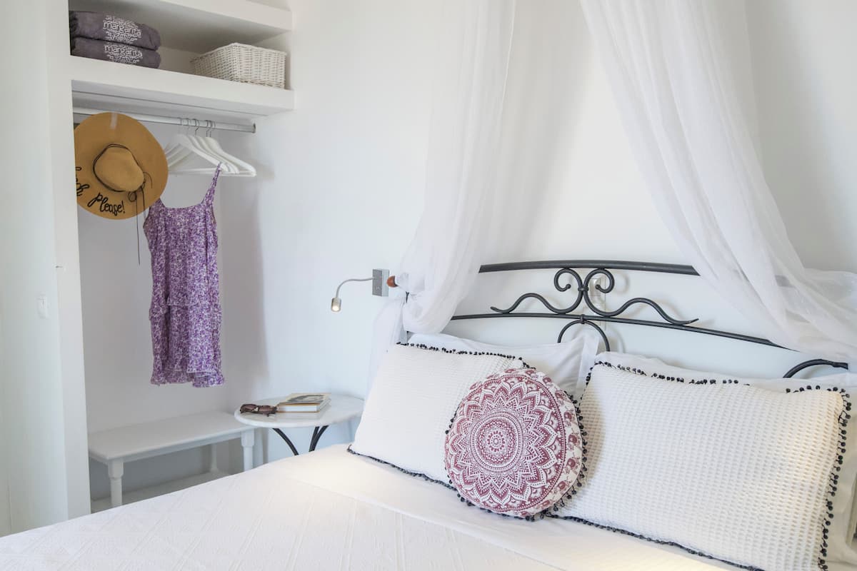 Ein ordentlich eingerichtetes Schlafzimmer mit einem Bett, einem Nachttisch, einem aufhängbaren Hut und einer Ablage mit gefalteten Handtüchern.