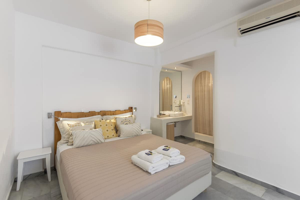 Ein modernes Hotelzimmer mit einem großen Bett, Nachttisch und einem Badezimmer mit Spiegel und Waschbecken.