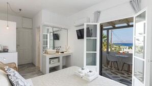 Un dormitorio moderno con una cama grande, un baño con lavamanos y espejo, y un balcón con vista al mar.