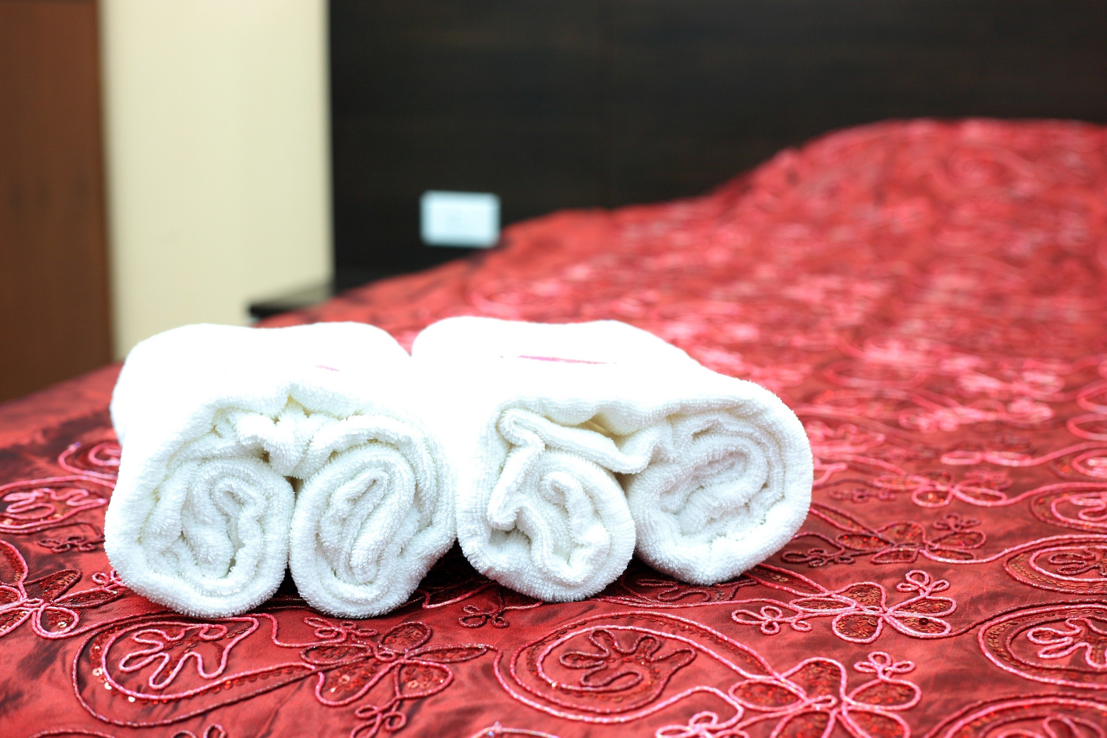 Un lit recouvert d’une couvre-lit rouge à motifs, avec deux serviettes blanches roulées posées dessus.