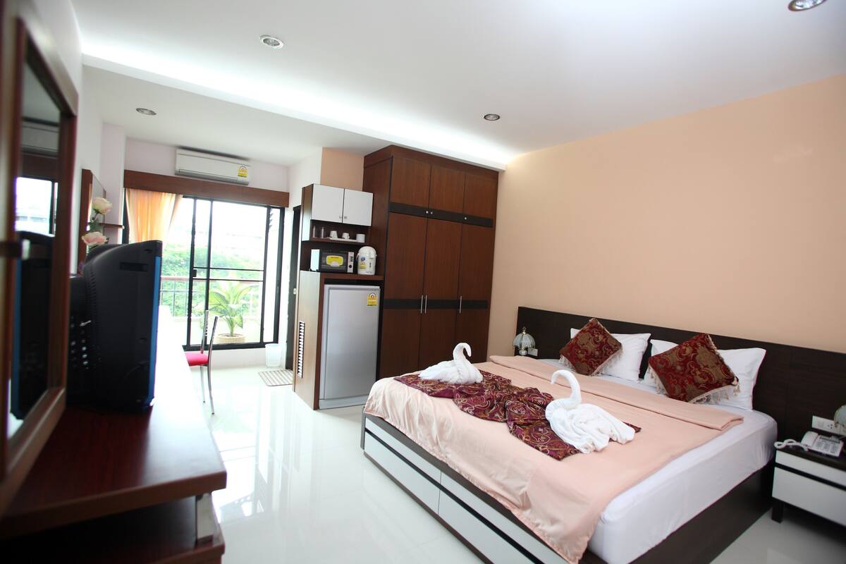 A hotel room with a bed, a desk with a computer, a wardrobe, and a view of the outdoors.