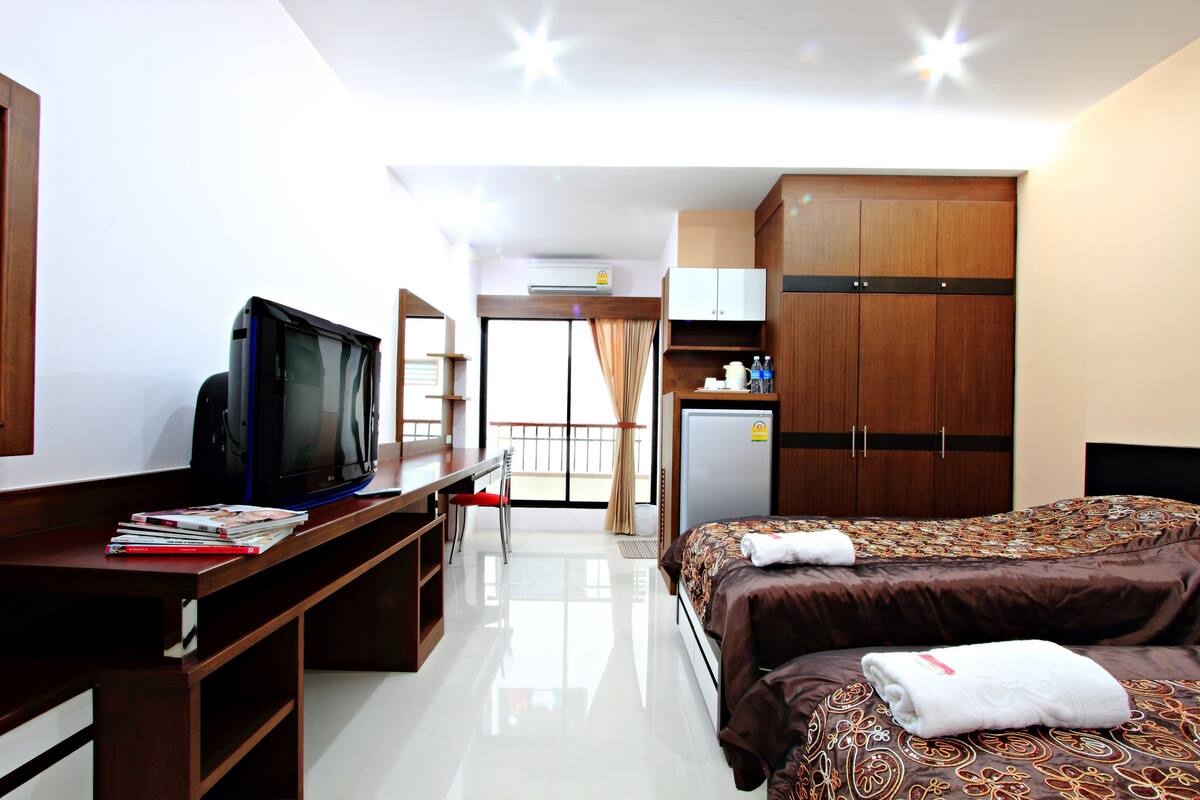A hotel room with a bed, a desk with a television, a wardrobe, and a kitchenette.