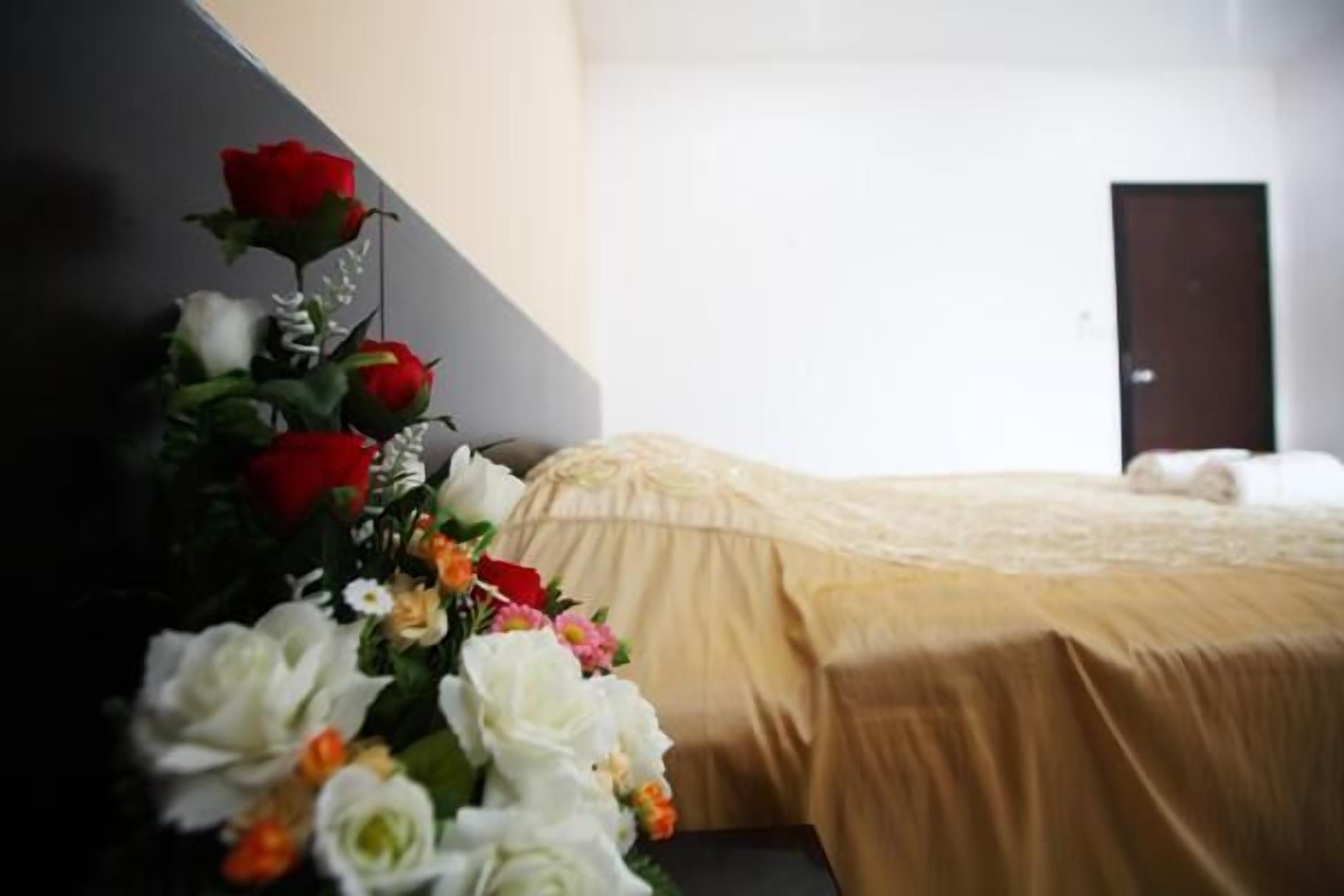 Habitación de hotel con una cama cubierta con sábanas color beige, un cabecero oscuro y un arreglo floral en la pared con diversas flores.