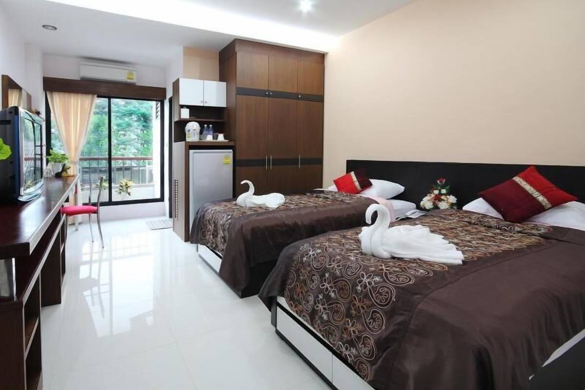 A hotel room with two beds, a desk, a TV, a wardrobe, and a balcony with a view.