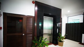 A modern elevator with a metallic finish, a wooden door with horizontal slats, and two potted plants on a tiled floor. - Pattara Place (Chiang Mai)