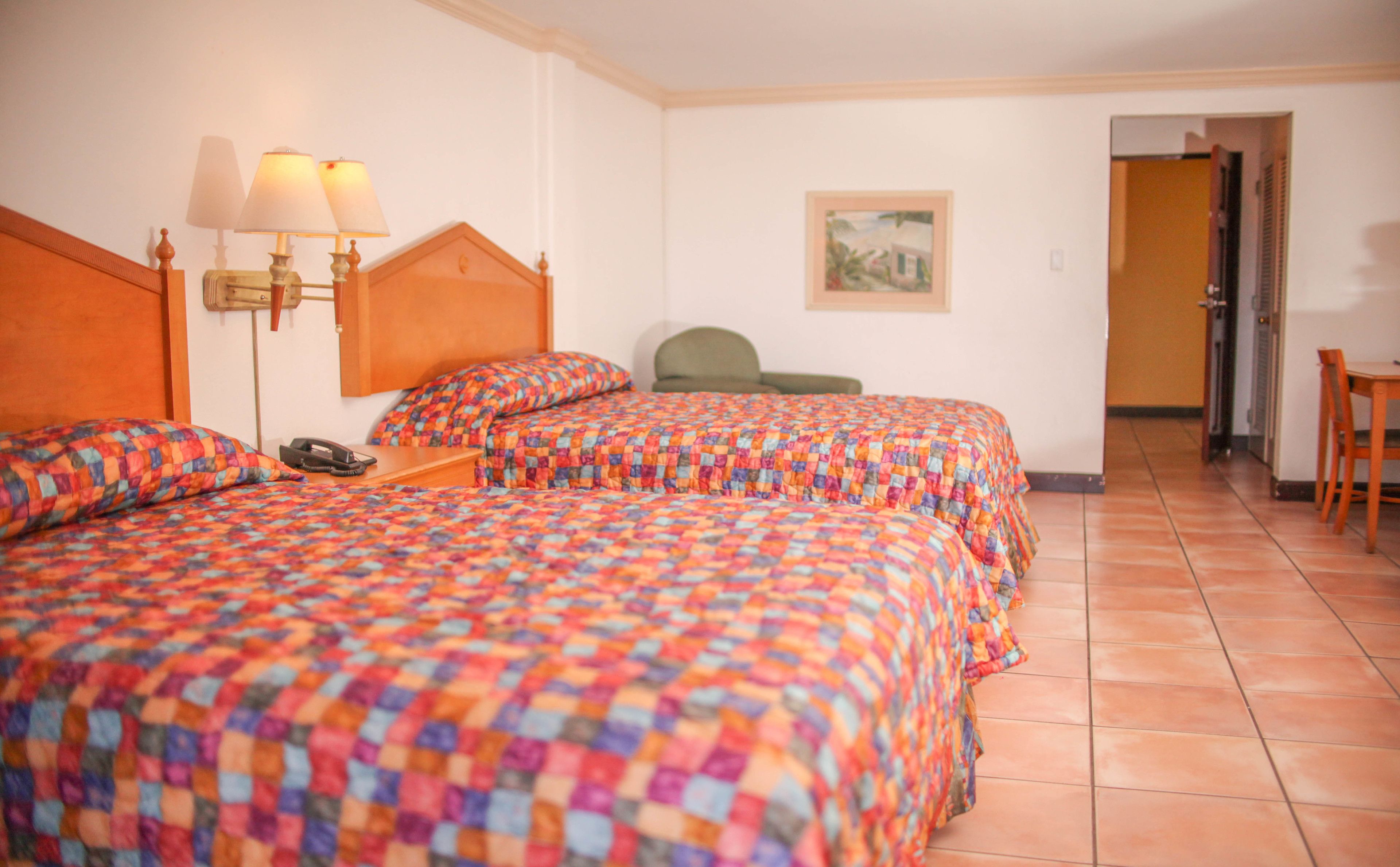 A hotel room with two beds, a chair, a desk, and a painting on the wall.