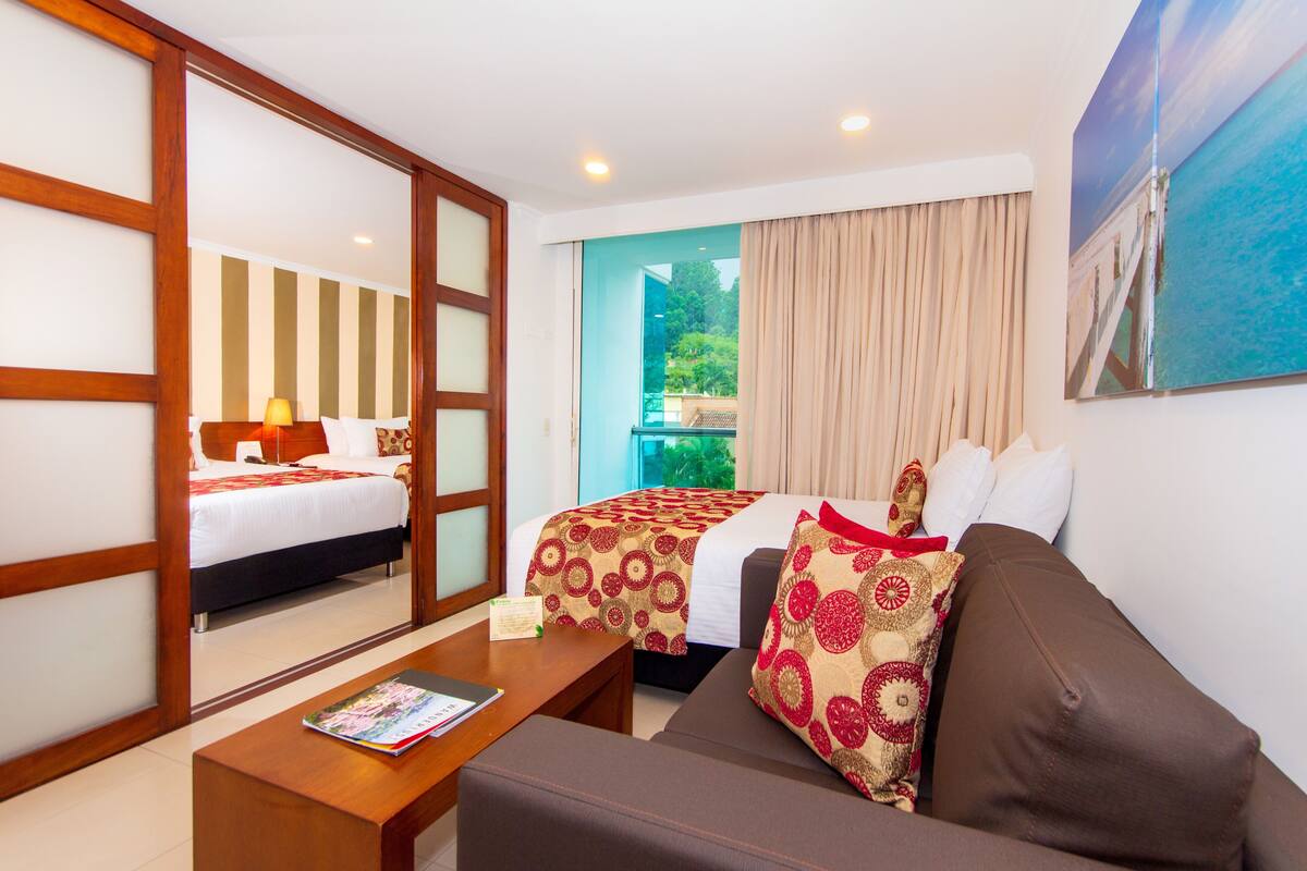 A hotel room with a bed, a sofa, a coffee table, and a large window with curtains.